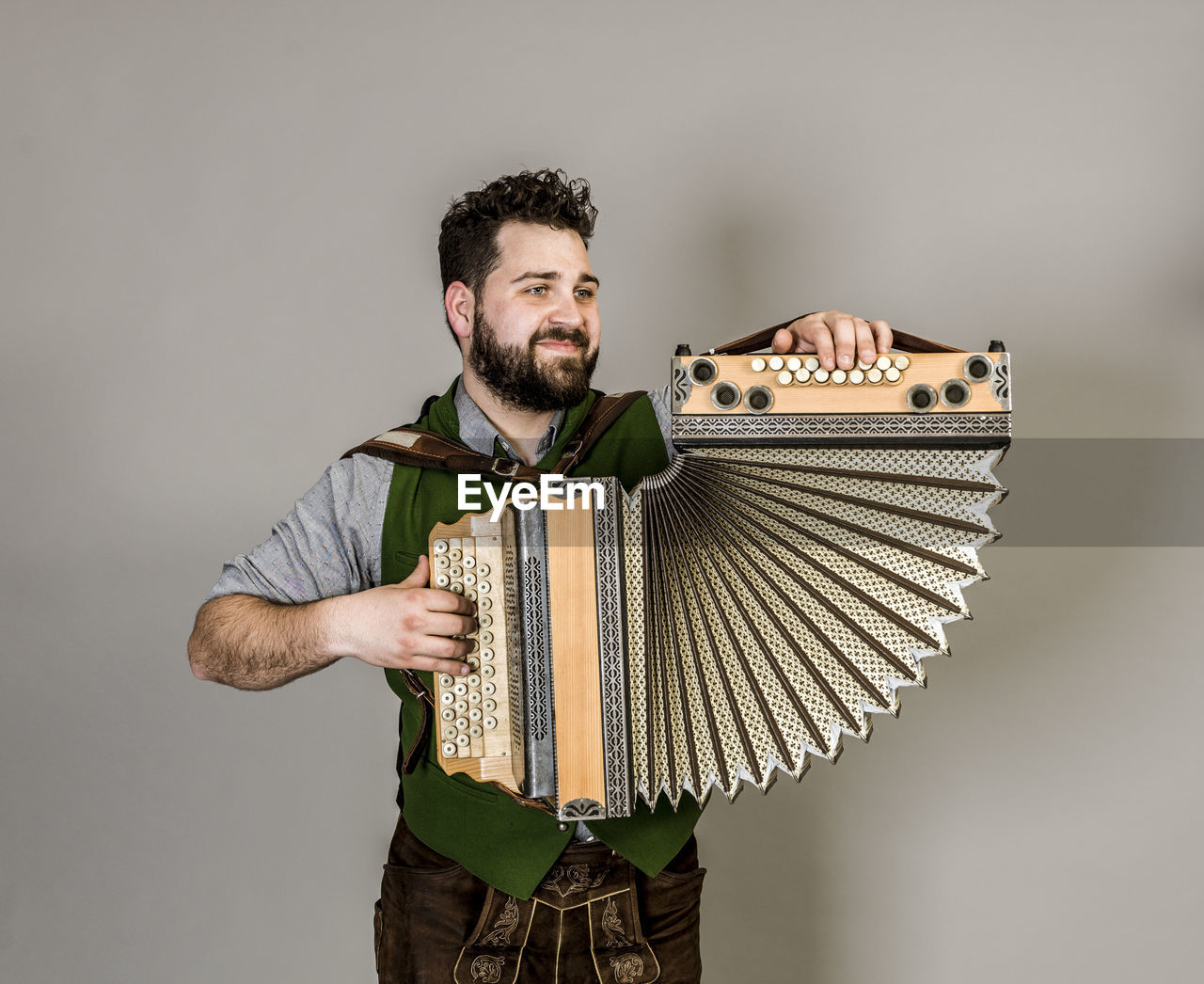 Smiling young man playing accordion against gray background