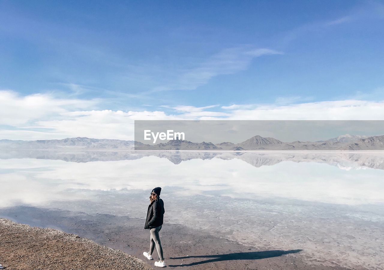 Woman walking on lakeshore against blue sky