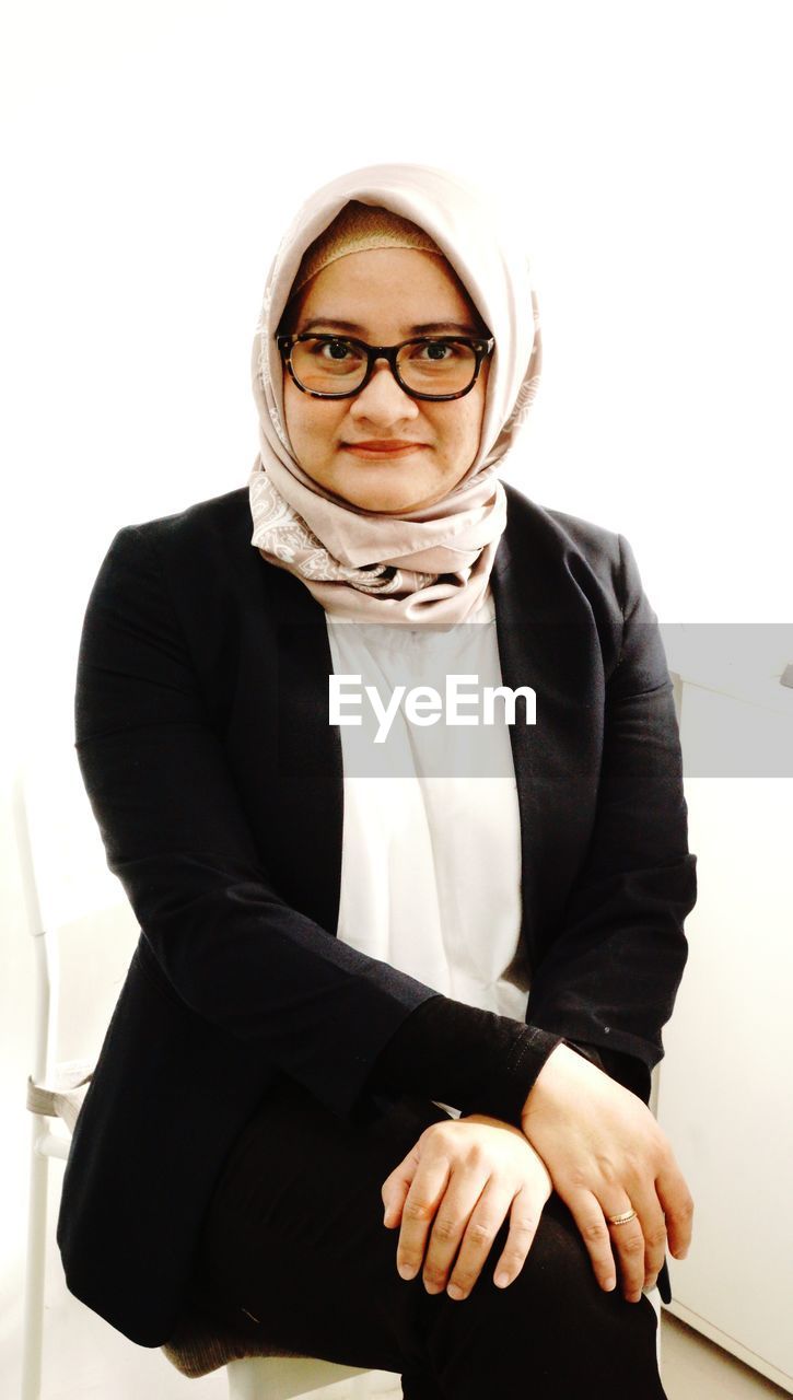 adult, one person, portrait, eyeglasses, business, looking at camera, glasses, clothing, formal wear, scarf, women, outerwear, indoors, tuxedo, person, businesswoman, human face, female, young adult, front view, eyewear, men, vision care, business finance and industry, fashion accessory, occupation, white background, hijab, emotion, smiling, studio shot, fashion, lifestyles