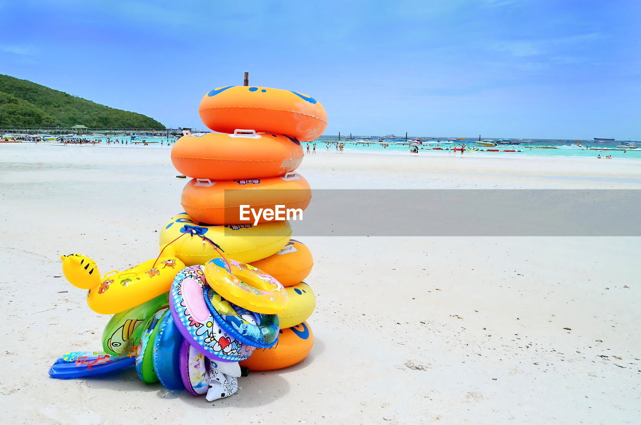 Stacked colorful inflatable rings at sandy beach against sky