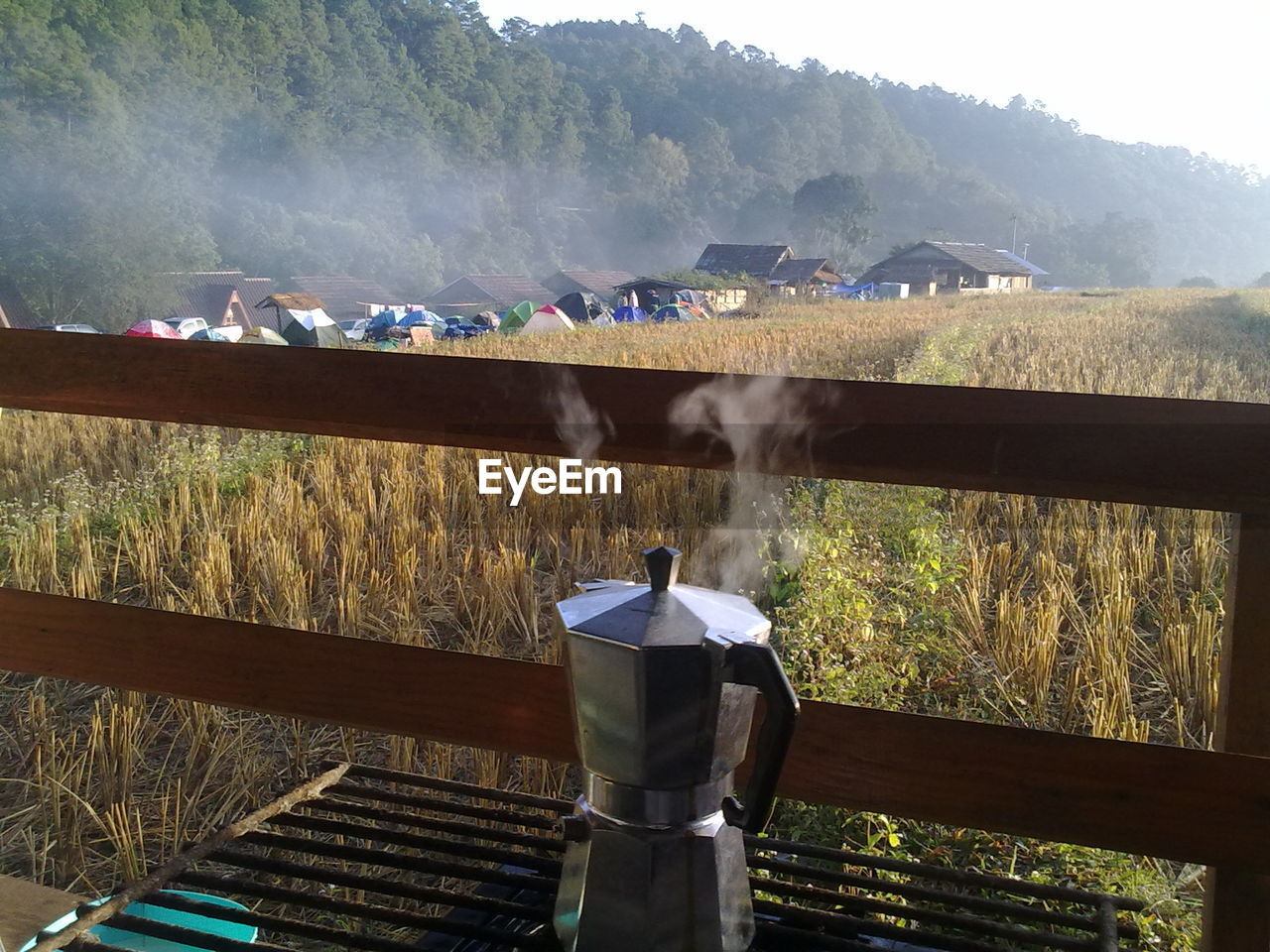 Hot coffee maker on metal grate by grassy field