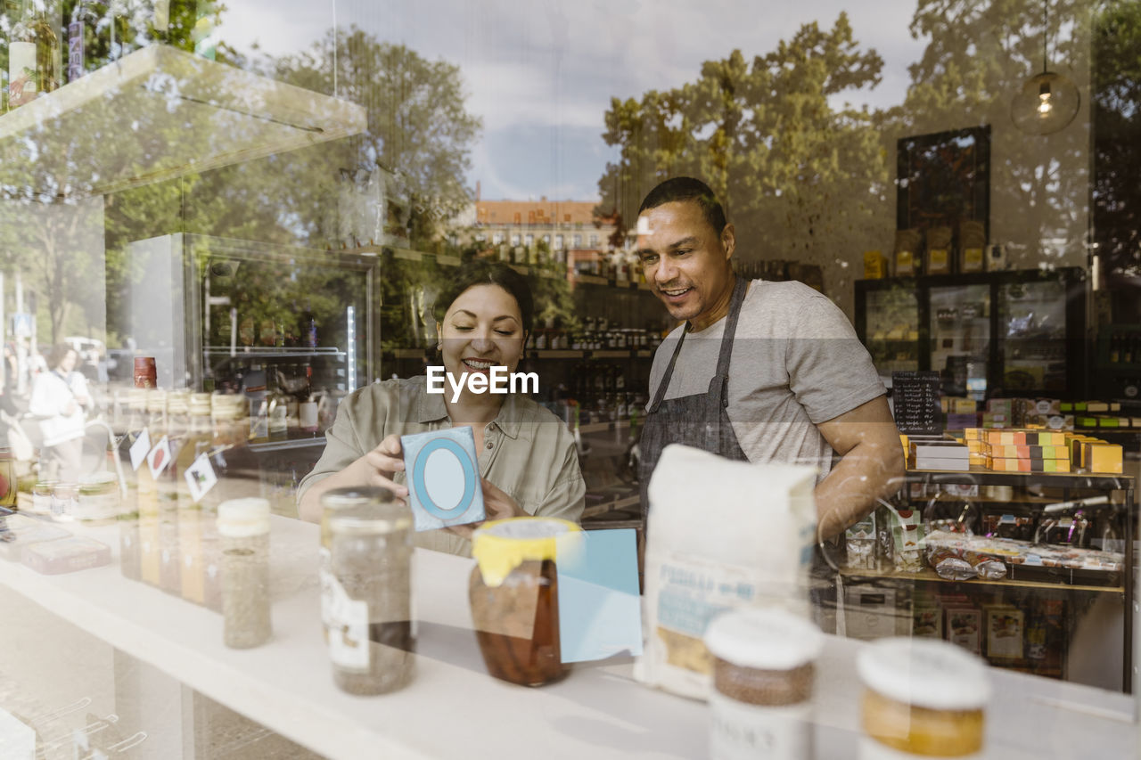 Happy owners discussing over merchandise in store seen through glass