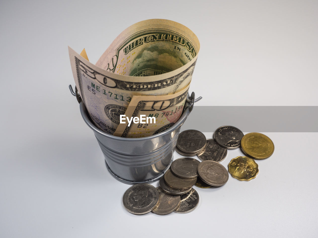 High angle view of paper currency in bucket by coins against gray background