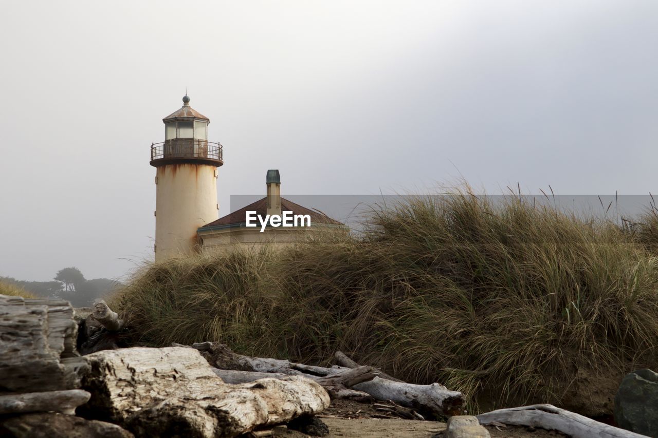 LIGHTHOUSE ON ROCK AMIDST BUILDINGS AGAINST SKY