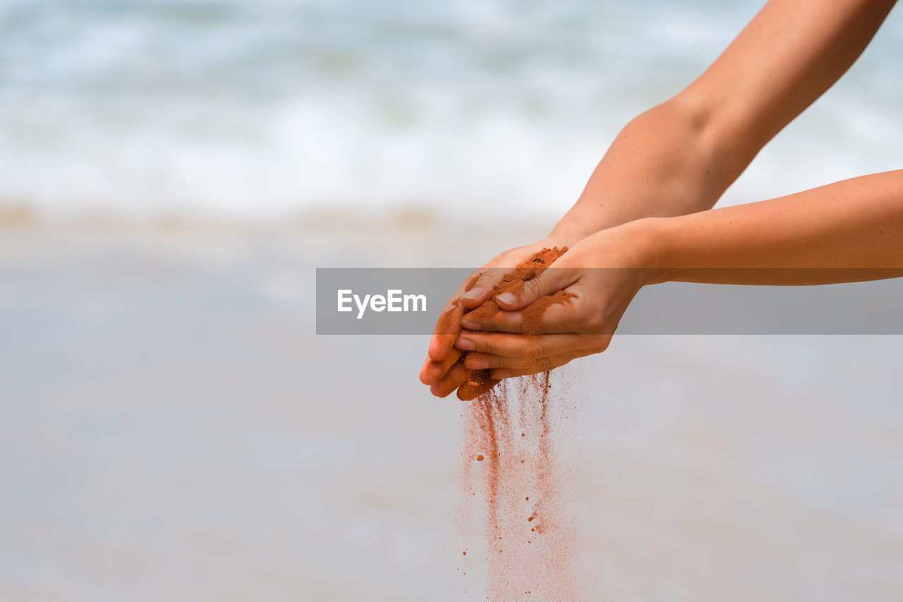 Cropped image of hands holding sand at beach