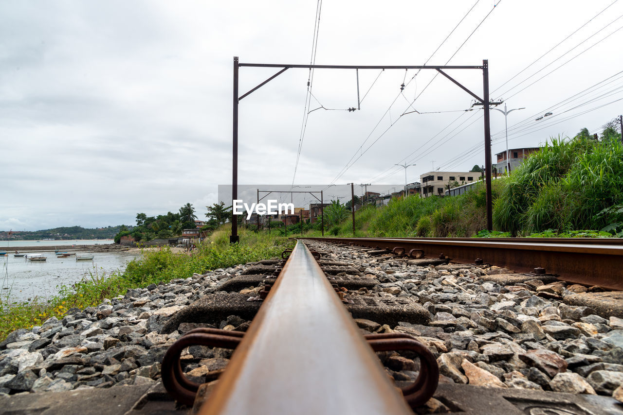 track, transport, sky, transportation, railroad track, nature, rail transportation, cloud, water, electricity, cable, mode of transportation, no people, railway, day, technology, electricity pylon, architecture, power line, outdoors, plant, vanishing point, rock, environment, travel, diminishing perspective, vehicle, land, power supply, sea, tree, the way forward, built structure, overcast, power generation