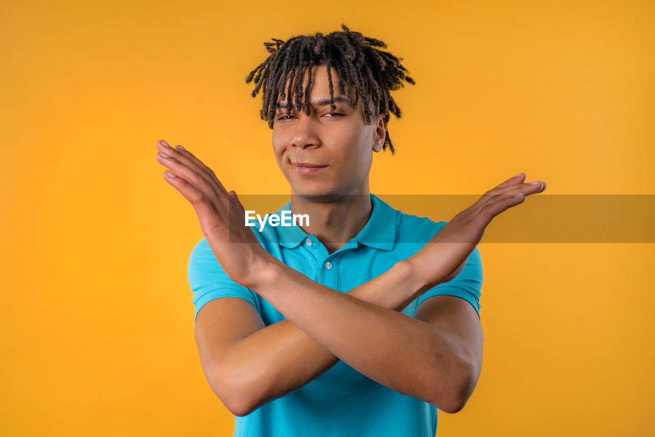 colored background, one person, studio shot, portrait, yellow, adult, yellow background, waist up, emotion, young adult, indoors, men, smiling, orange color, sign language, orange background, looking at camera, person, teenager, hand, copy space, arm, happiness, lifestyles, human face, front view, standing, gesturing, hairstyle, cut out, casual clothing, facial expression, photo shoot