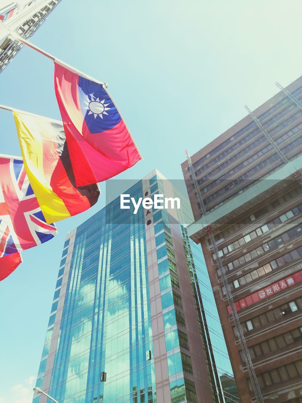 Low angle view of national flags by modern buildings in city against clear sky