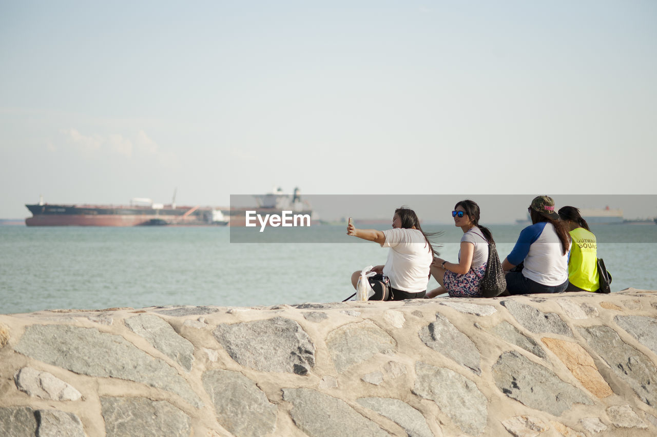 REAR VIEW OF TWO PEOPLE SITTING ON BEACH