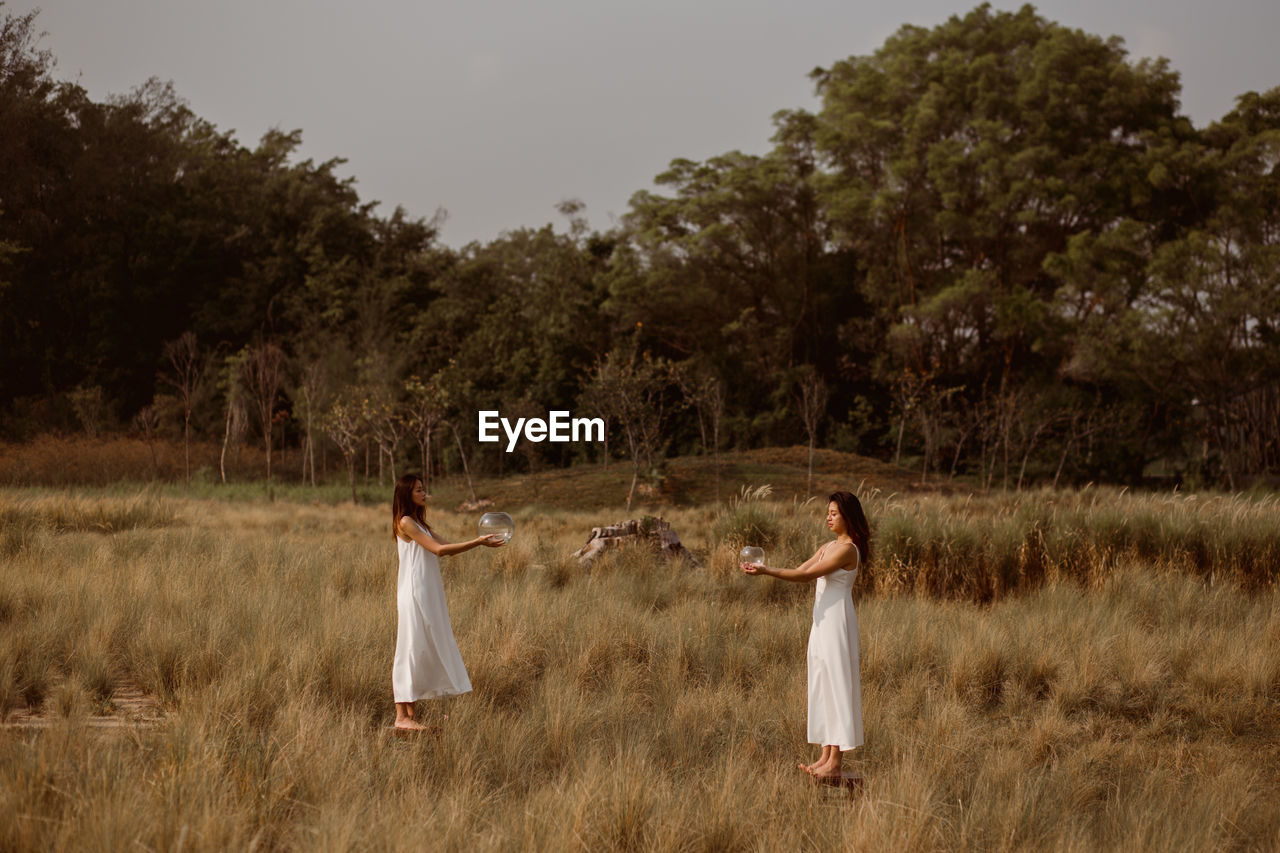 PEOPLE STANDING ON FIELD AGAINST TREES AND SKY