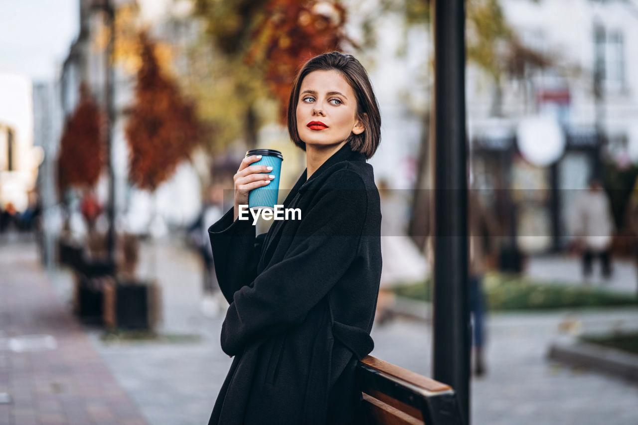 Portrait of young woman holding cup of coffee in city