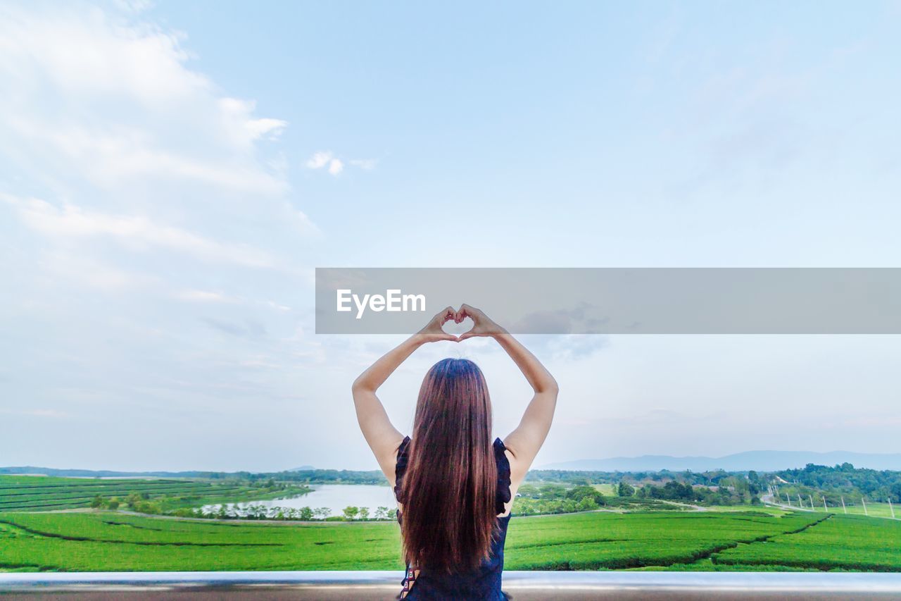 Rear view of woman making heart shape against land