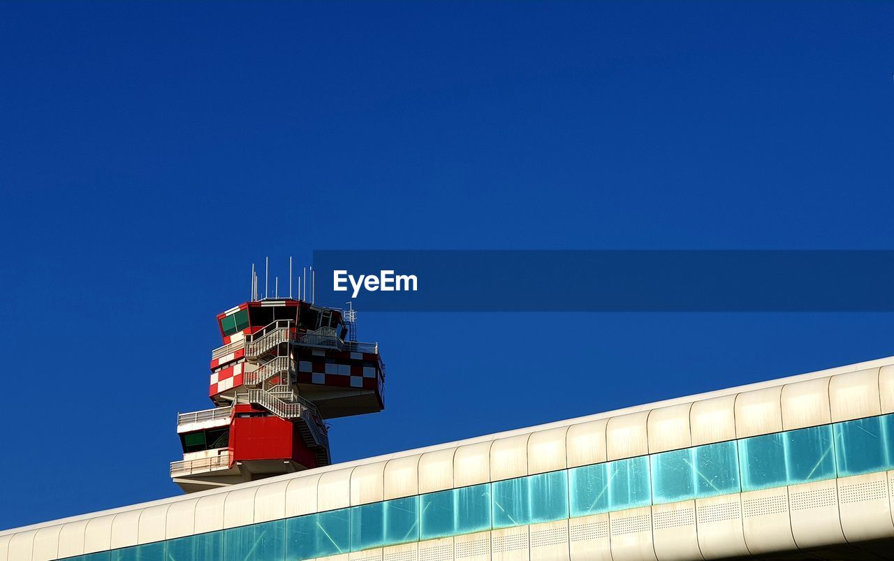 Low angle view of airport tower and building against clear blue sky