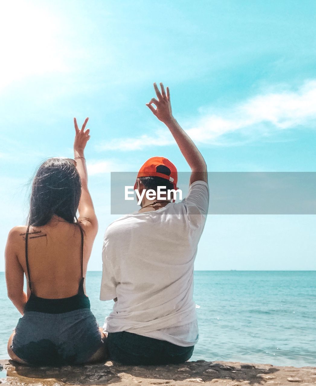 Rear view of people gesturing while sitting at beach against sky