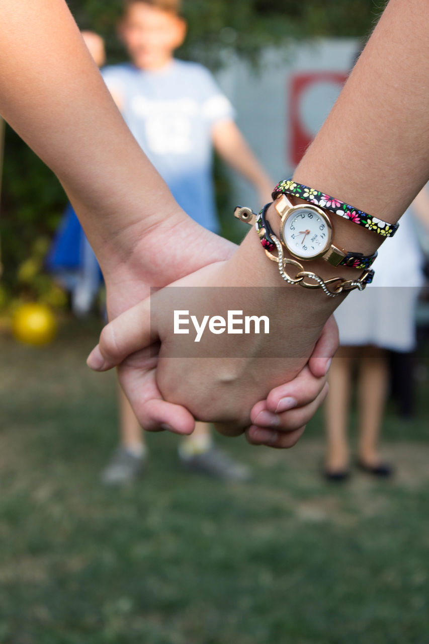 CLOSE-UP OF HAND HOLDING HANDS OVER BLURRED MOTION OF PEOPLE