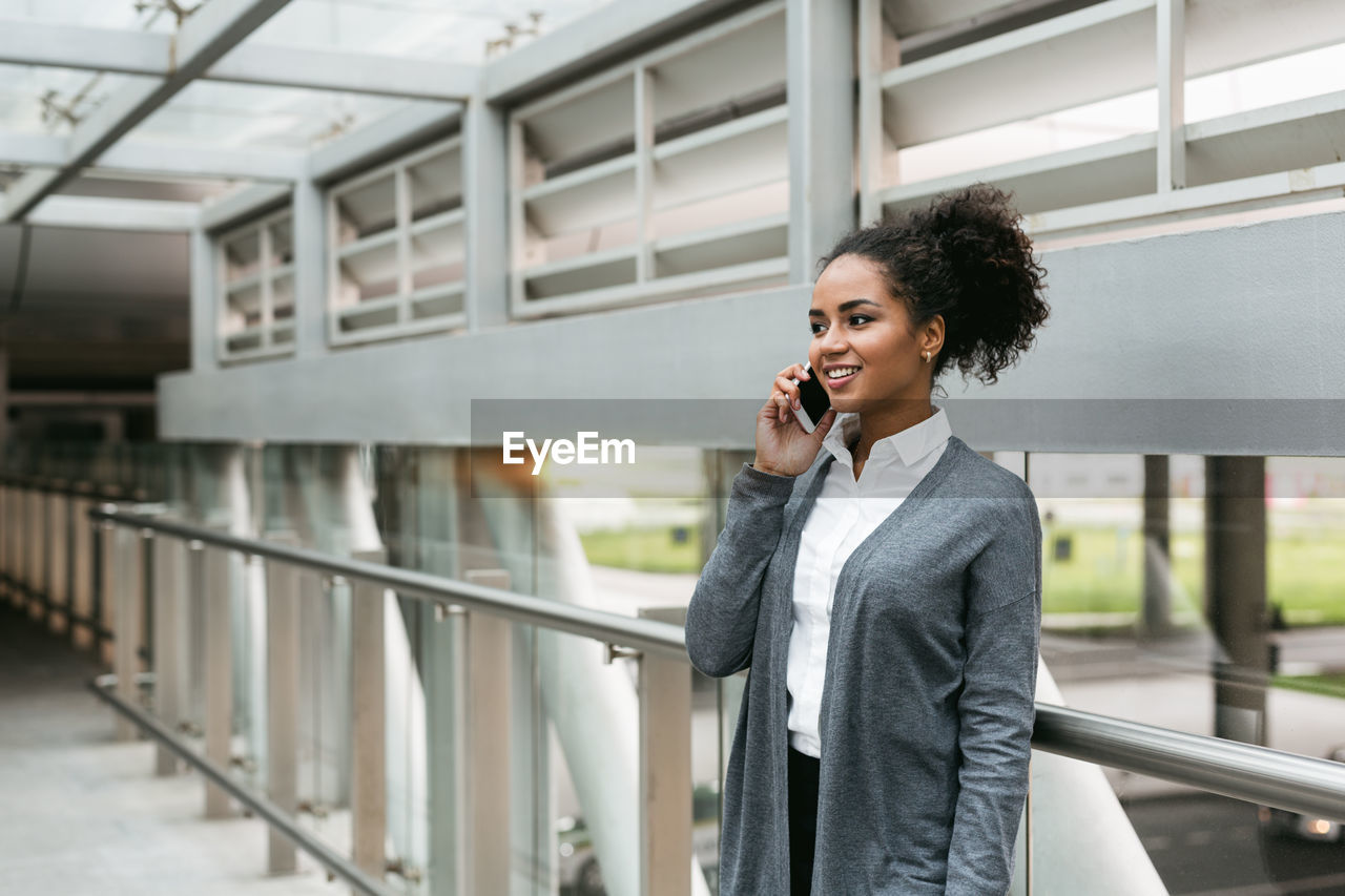 Businesswoman using phone while standing by railing