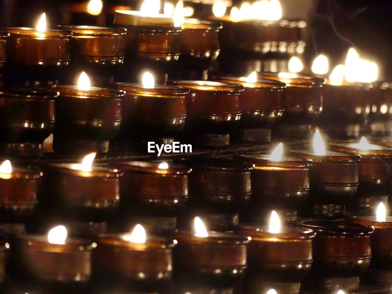 CLOSE-UP OF ILLUMINATED CANDLES BURNING IN ROW