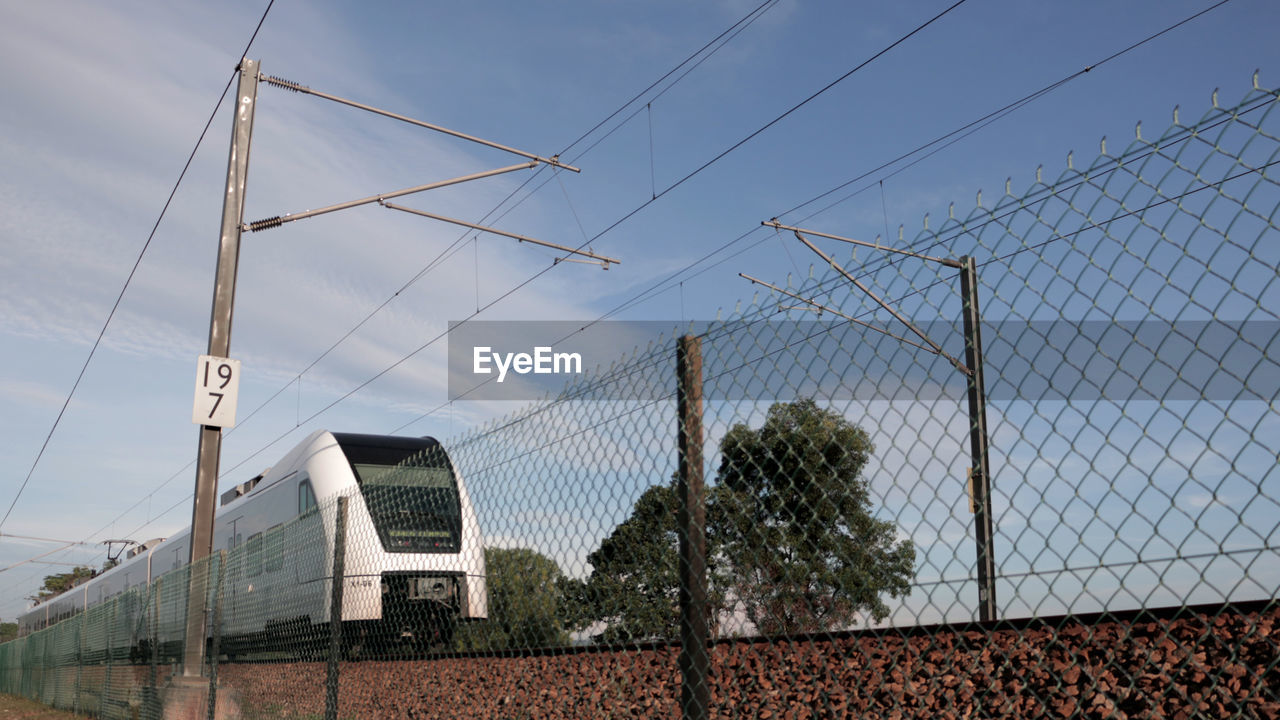 Low angle view of train by fence against sky