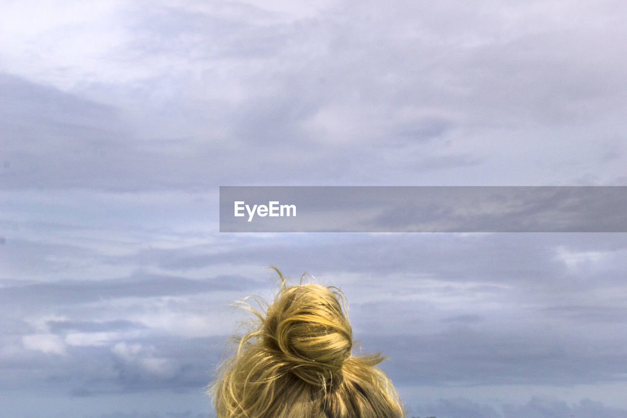 REAR VIEW OF WOMAN LOOKING AWAY AGAINST SKY