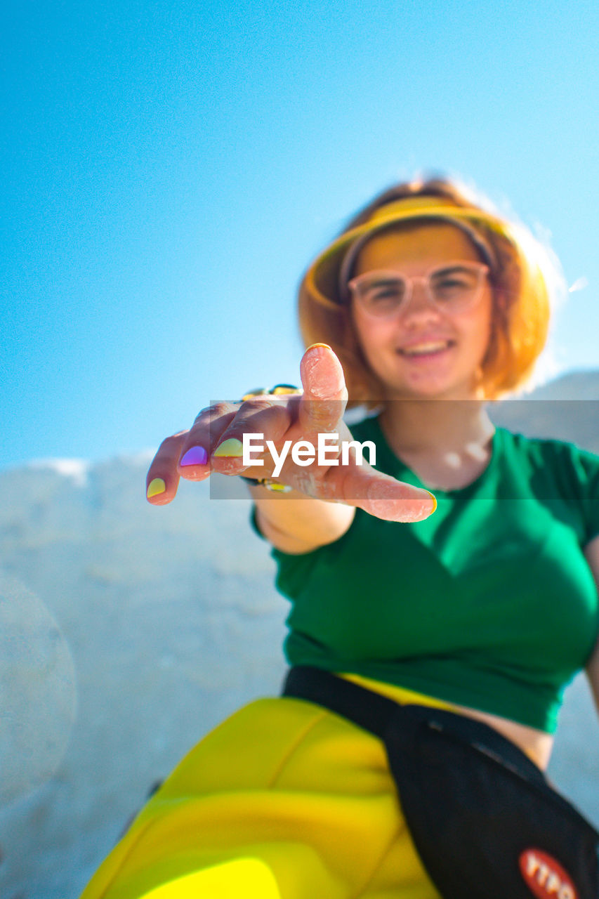 Portrait of smiling woman gesturing against clear blue sky