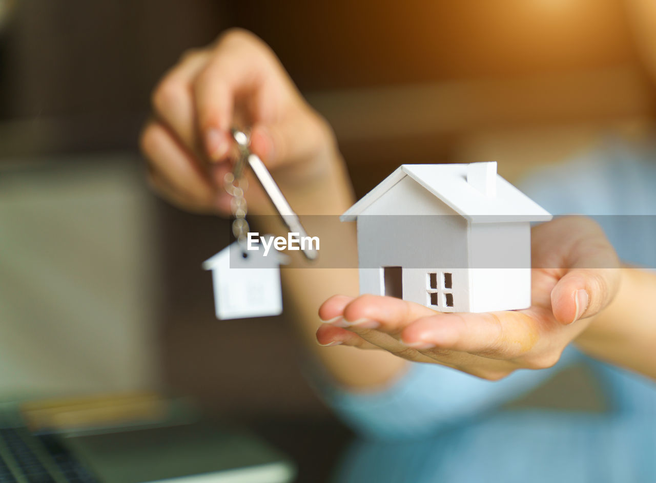 Woman holding white house model and house key in hand.mortgage loan and insurance concept.