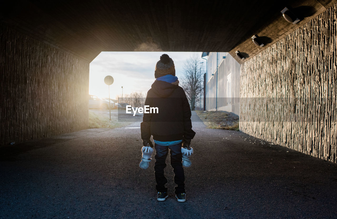 Young boy standing in a tunnel holding his ice skates in winter