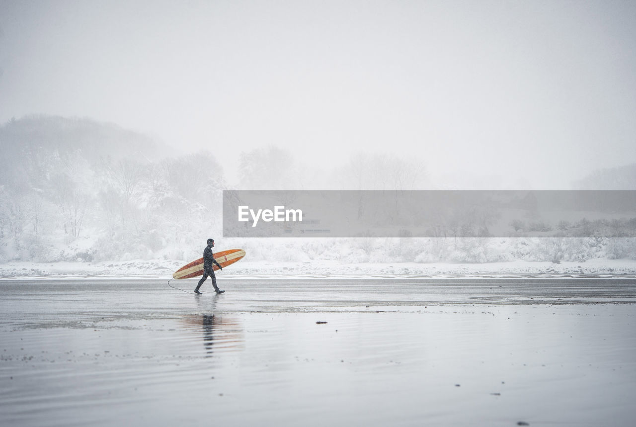 Surfer walking along the beach in maine during a winter snow storm