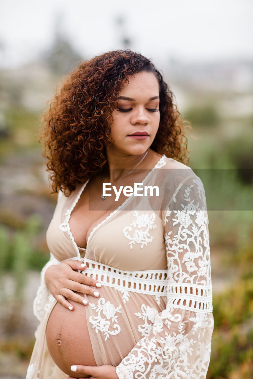 Young pregnant woman posing at beach in sheer dress