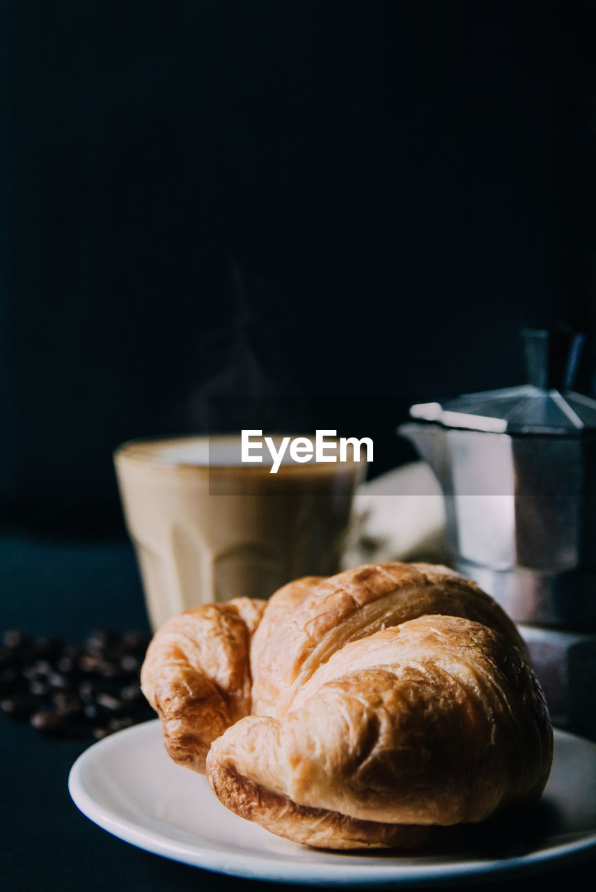 Croissant ,latte art ,and moka pot with roasted coffee on black background in the morning 