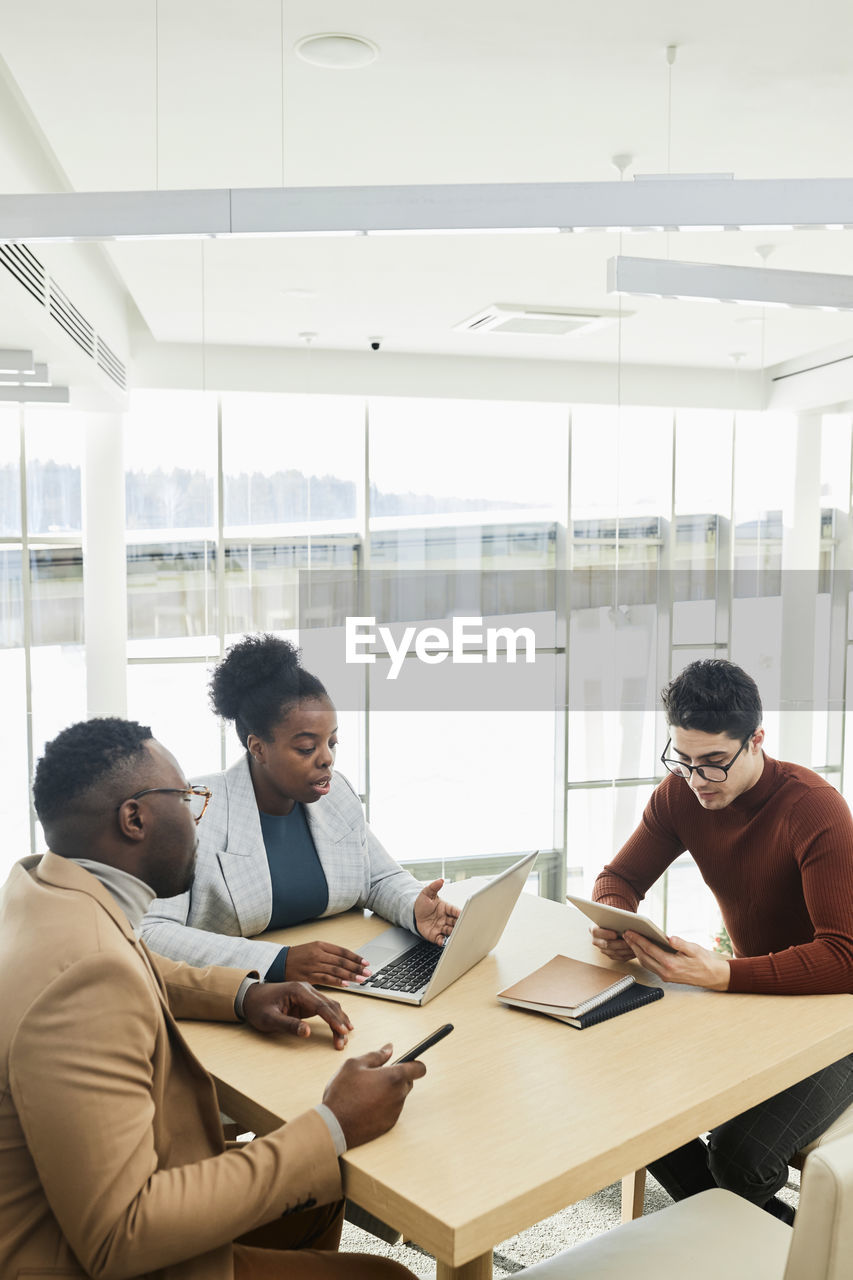 Young businesswoman discussing over laptop with colleagues sitting at desk in office