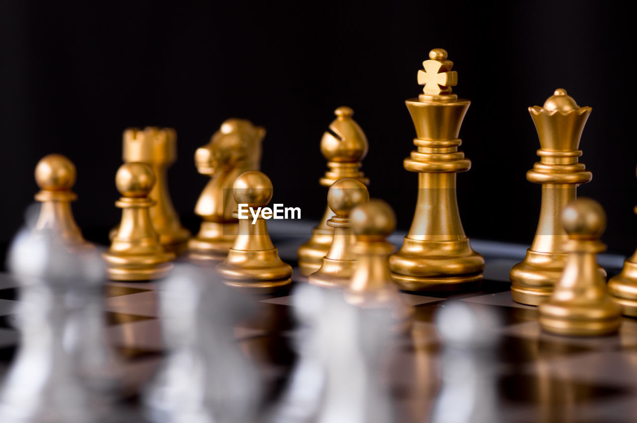 Close-up of golden chess pieces on board against black background