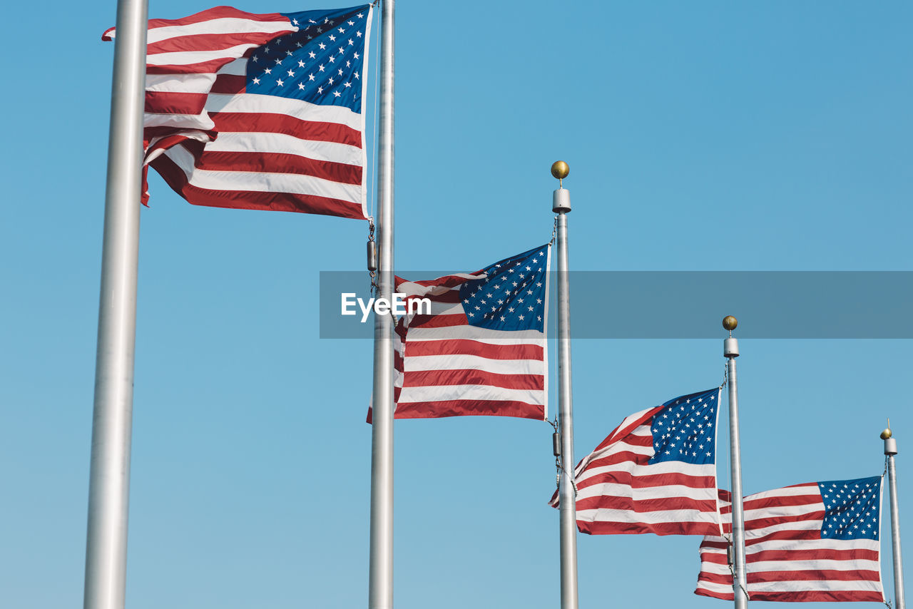 Low angle view of american flags fluttering against clear blue sky