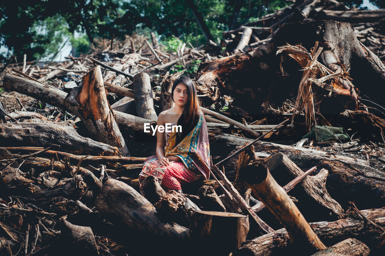 Portrait of young woman sitting on logs in forest