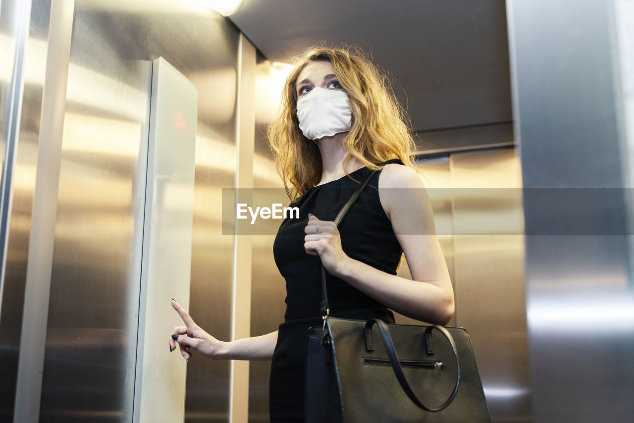 Low angle view of young woman wearing mask in elevator