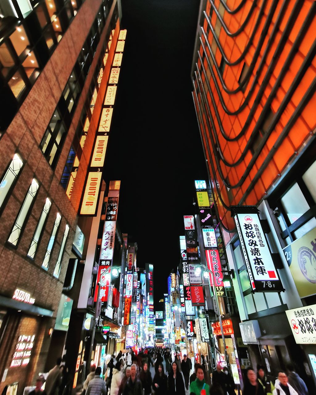 LOW ANGLE VIEW OF PEOPLE ON ILLUMINATED CITY BUILDINGS AT NIGHT