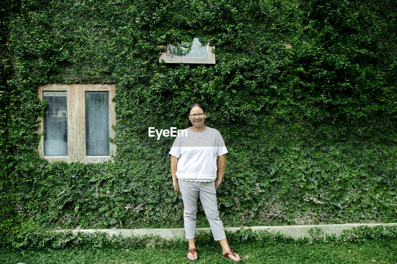 Portrait of woman standing against ivy