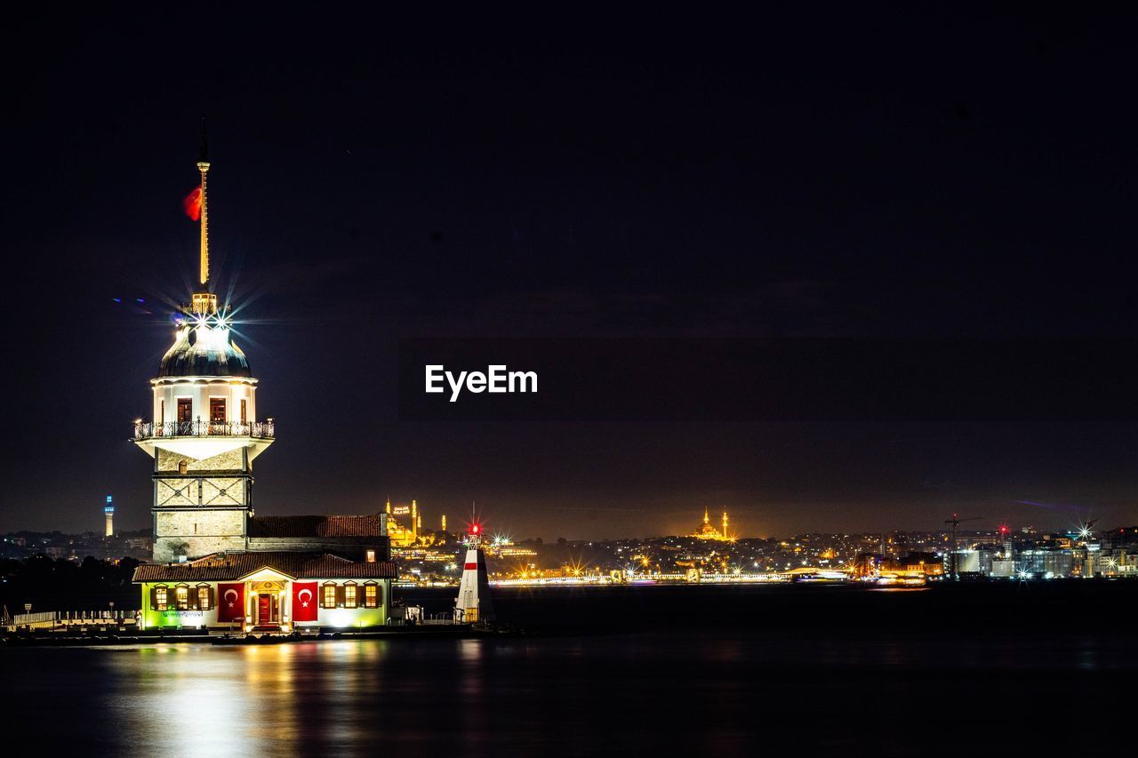 ILLUMINATED BUILDINGS BY RIVER AT NIGHT