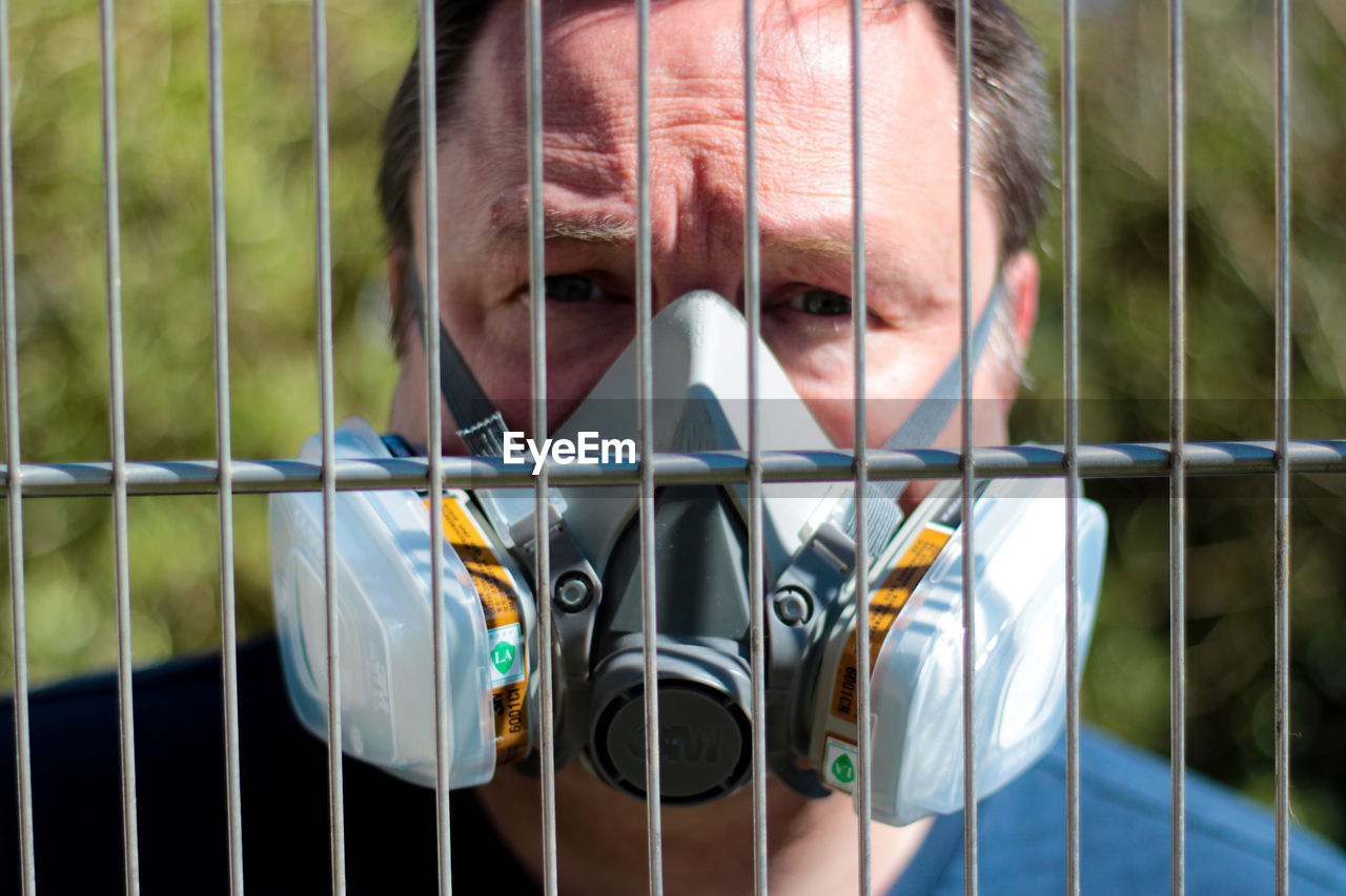 Portrait of man wearing mask seen through fence