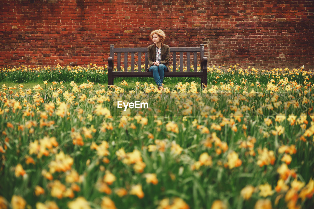 Woman sitting on bench amidst flowerbed in park