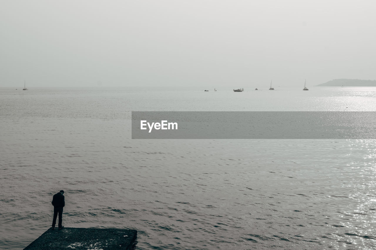 Silhouette person at sea against clear sky