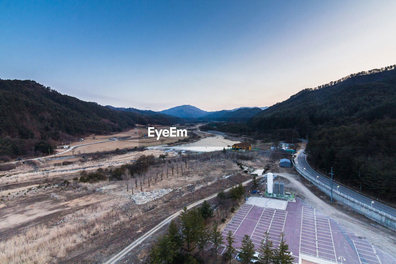 HIGH ANGLE VIEW OF ROAD BY RIVER AGAINST MOUNTAINS