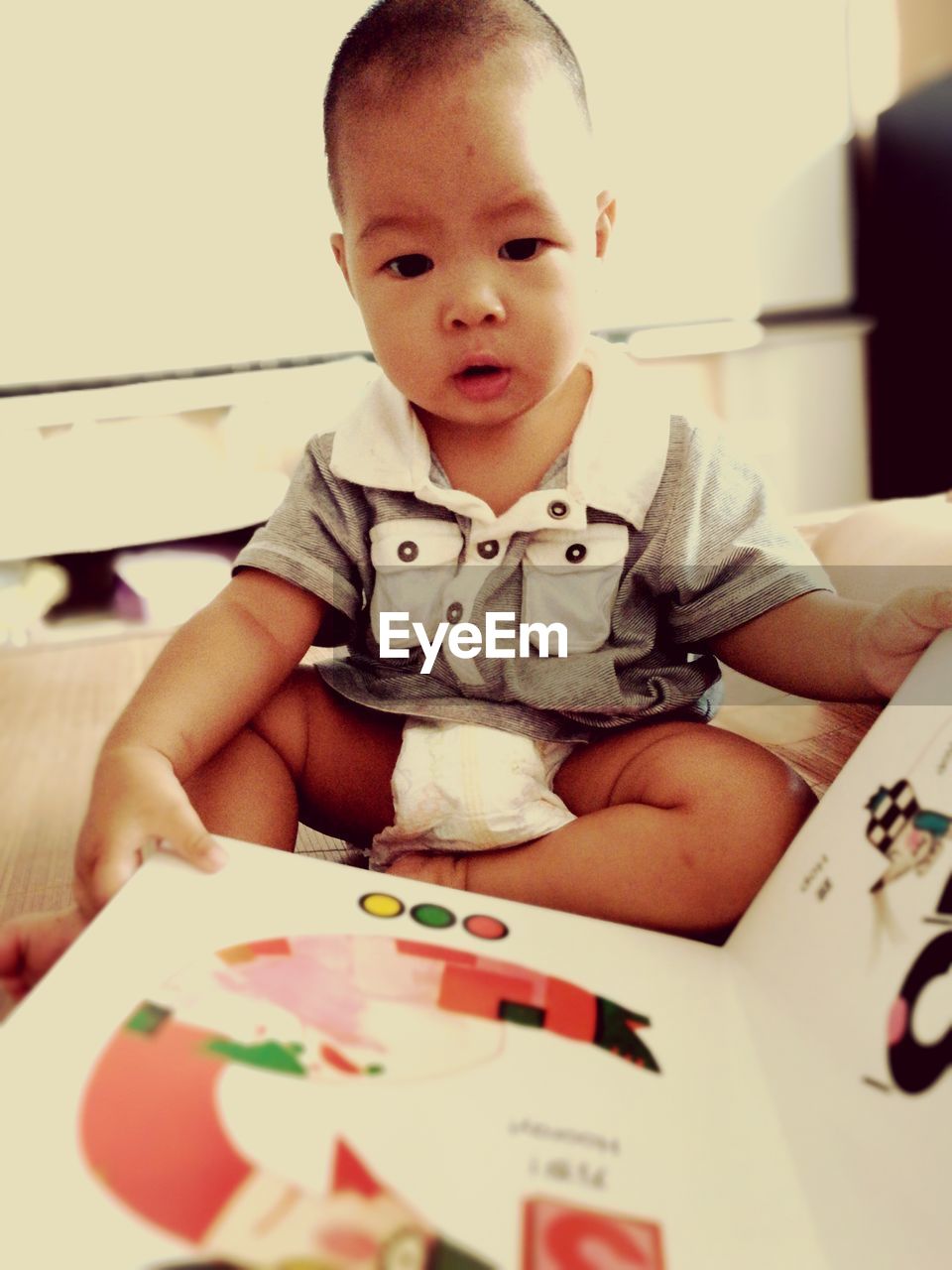 Baby boy with book sitting on bed at home