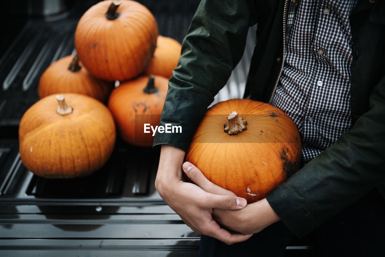 Midsection of man holding pumpkin while sitting outdoors