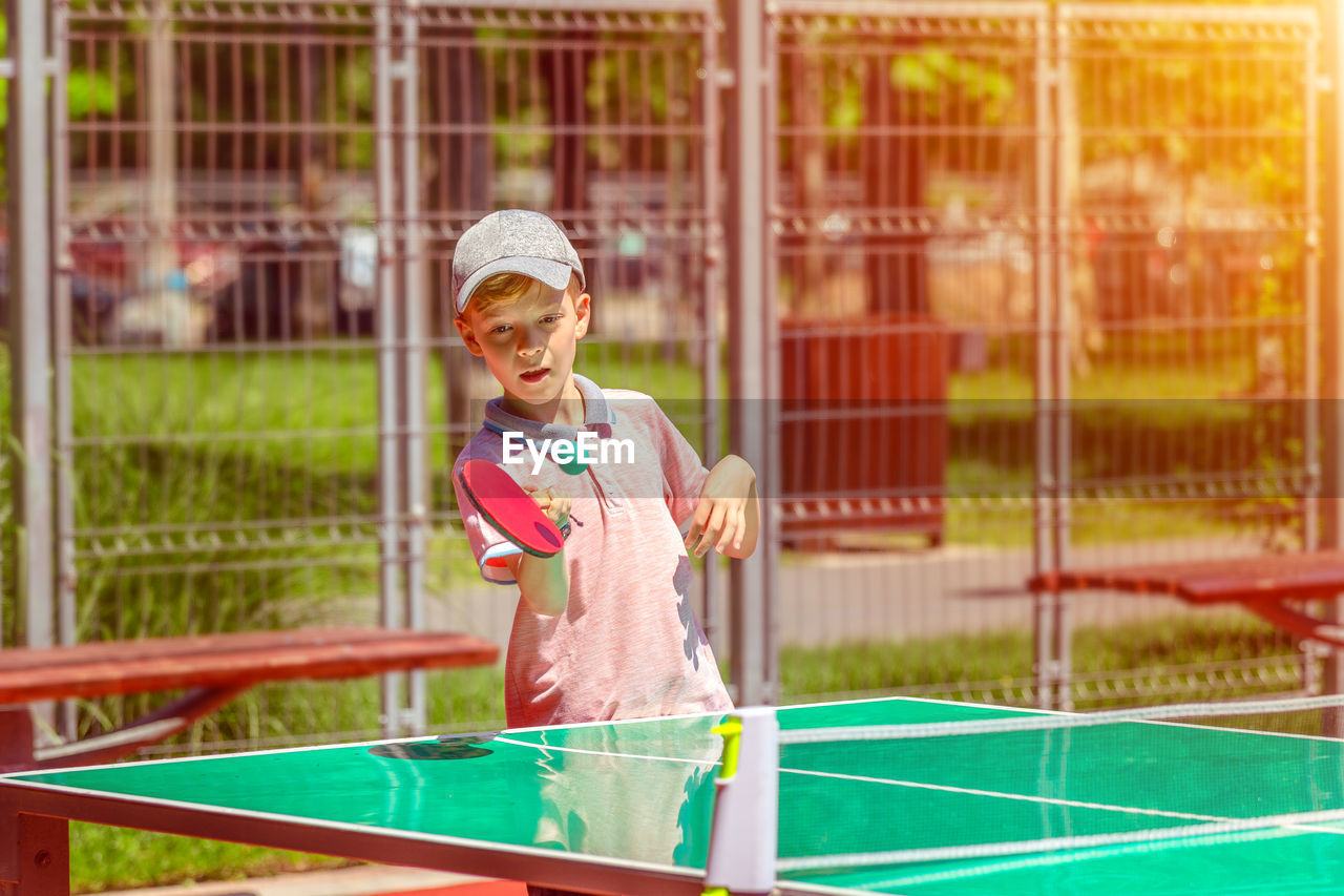 Boy playing table tennis during sunny day
