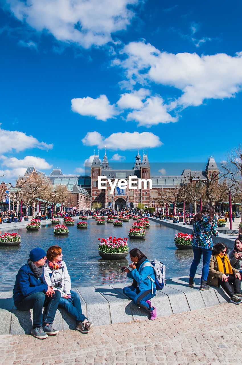 PEOPLE SITTING ON RIVERBANK AGAINST SKY