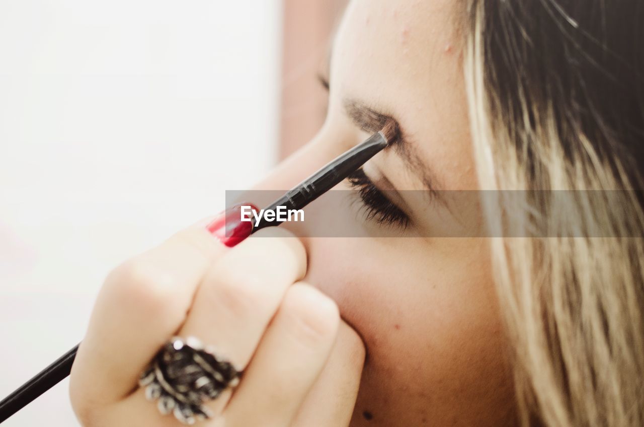 Close-up of young woman applying make-up on eyebrow