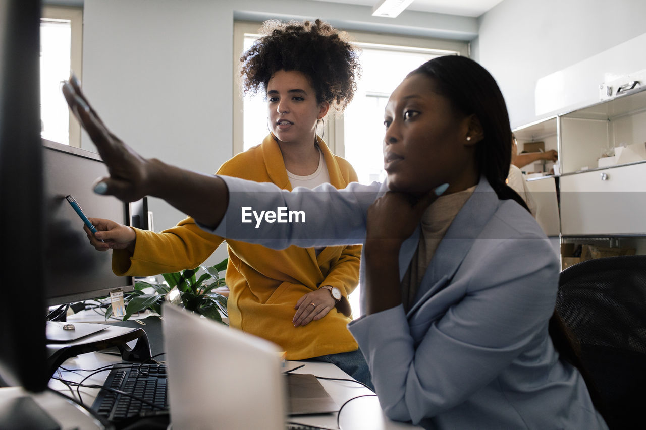 Businesswoman discussing with female colleague while working at coworking office