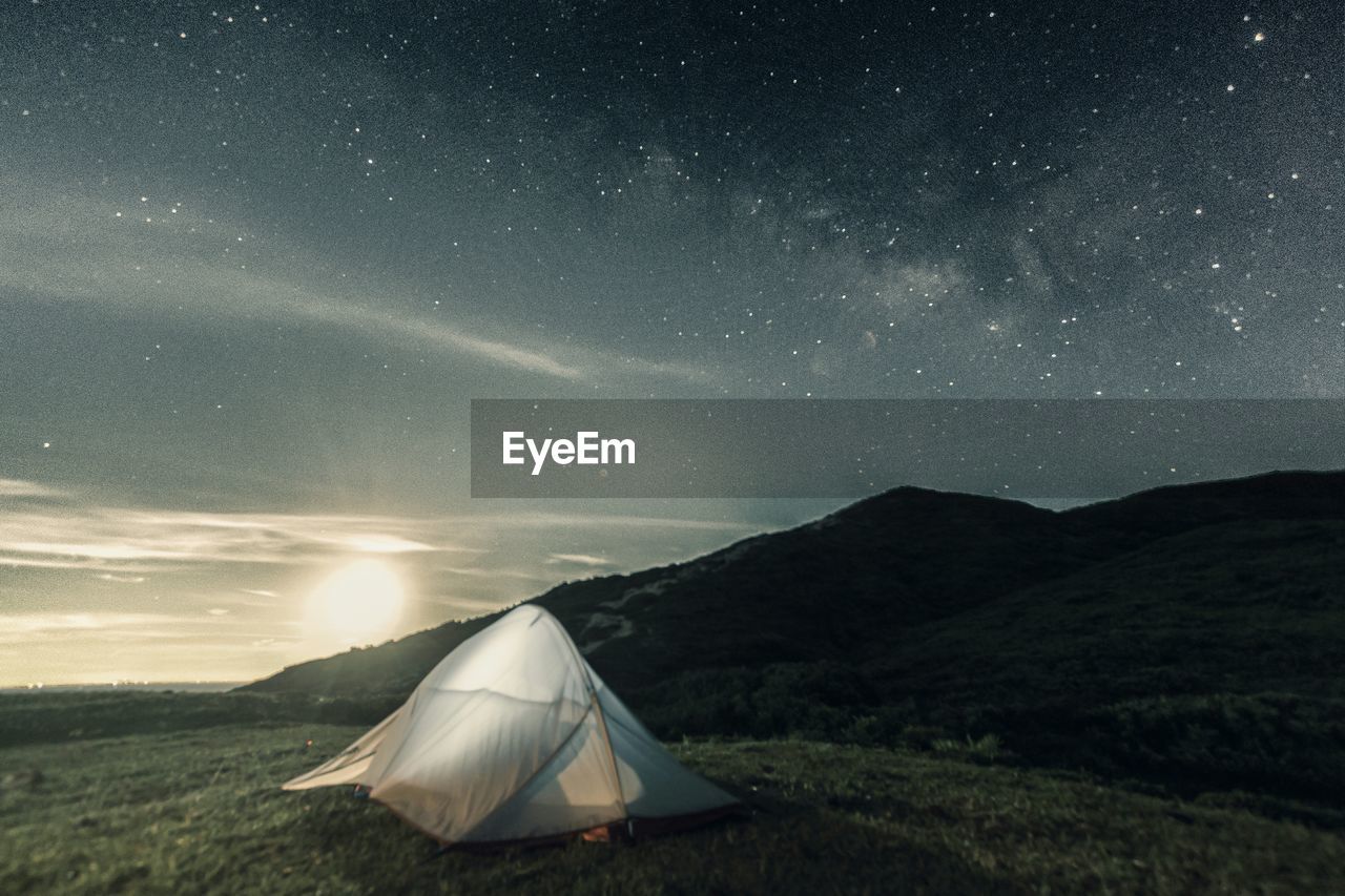 Tent on grassy field at mountain against starry sky