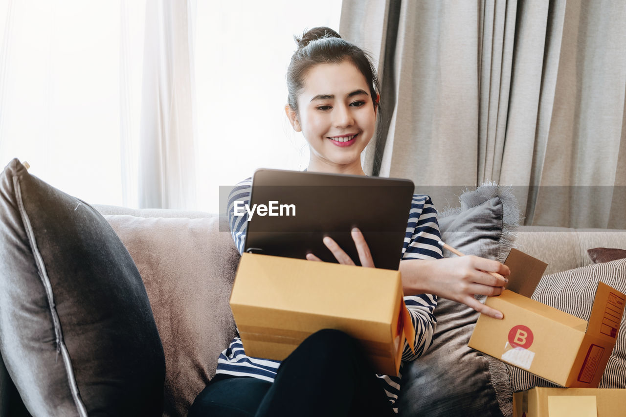 portrait of young woman using laptop while sitting on sofa at home