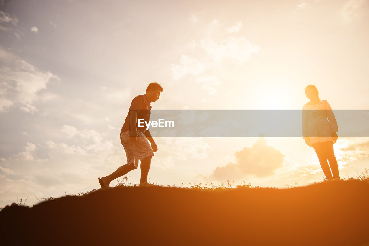 COUPLE WALKING ON FIELD AGAINST SKY DURING SUNSET